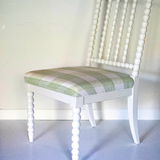 A white bobbin chair with a green plaid seat.