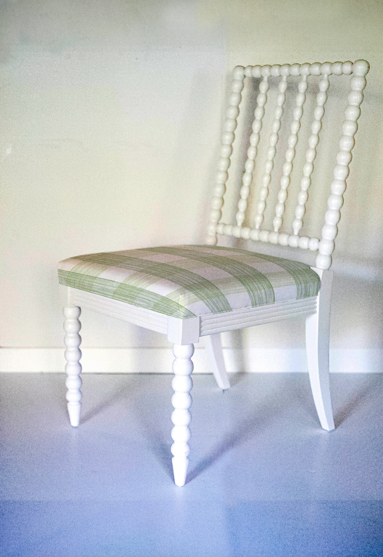 A white bobbin chair with a green plaid seat.