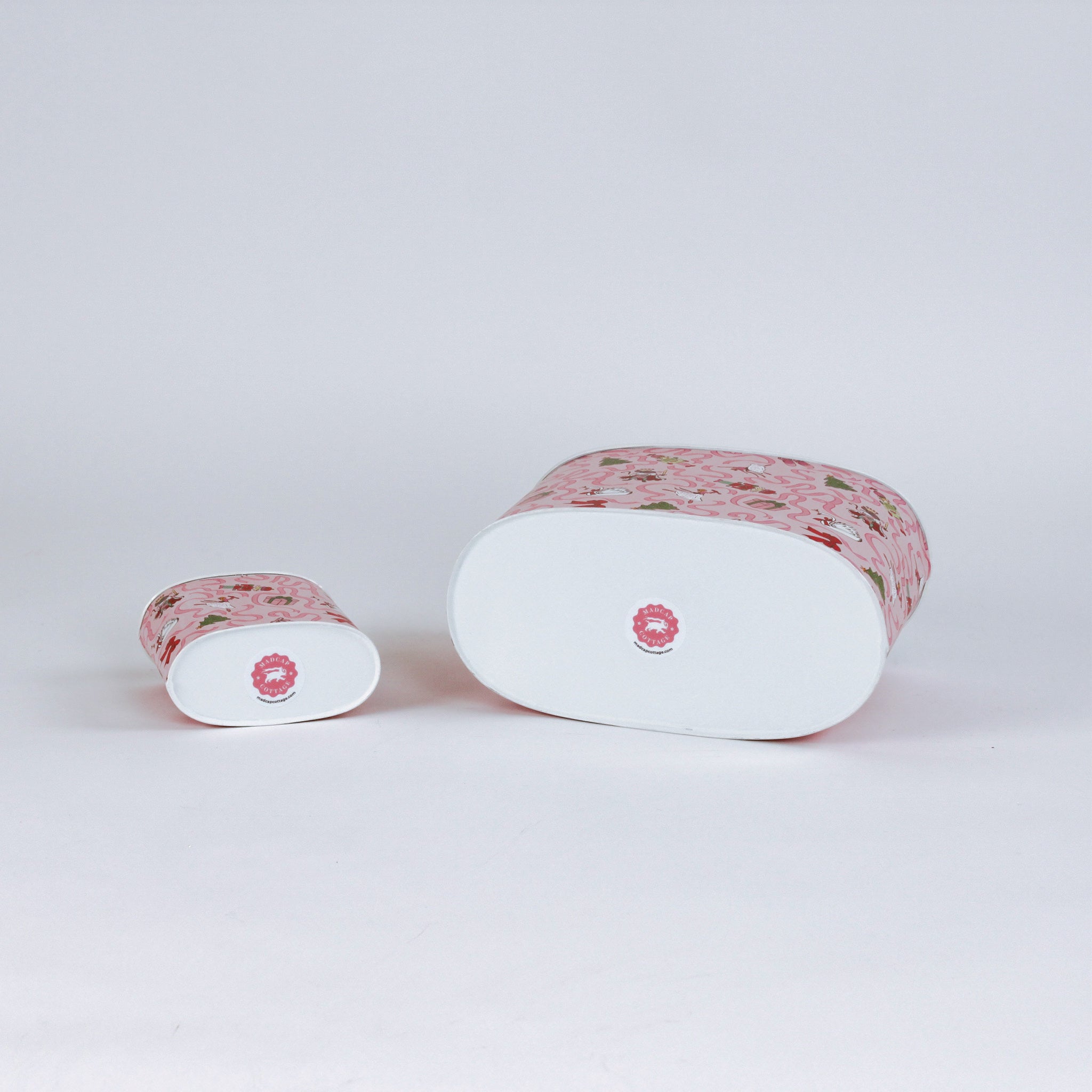 Two cylindrical christmas caddies with pink nutcracker patterns on a light gray background