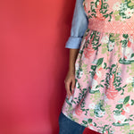 a woman wearing a pink and green chinoiserie apron featuring the Imperial Palace pattern from madcap cottage