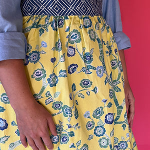 a woman wearing a yellow and blue chinoiserie apron featuring the Temple Garden pattern fabric from madcap cottage