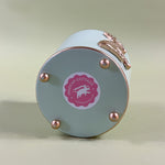 the bottom side of a green tole cachepot with a pink madcap cottage sticker on it