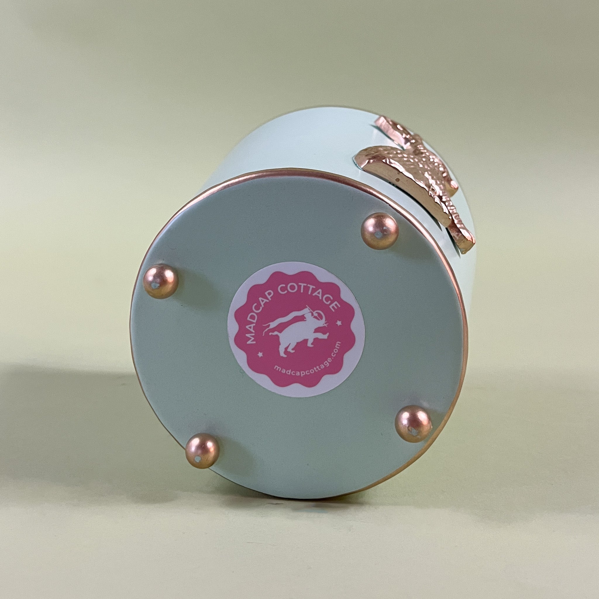 the bottom side of a green tole cachepot with a pink madcap cottage sticker on it