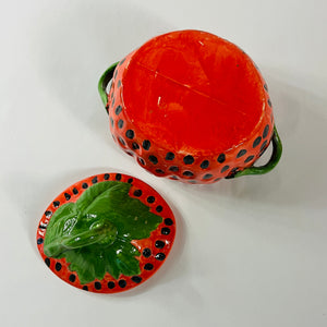 the underside of a large red vintage strawberry dish with a green handles and green detail on lid