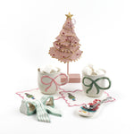 Two ceramic mugs with decorative handles, a small Christmas tree, and a spoon on a white background.