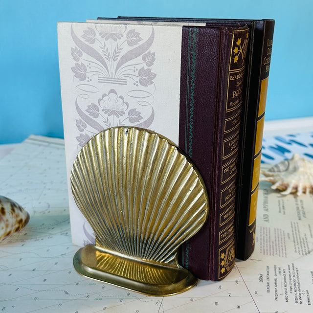 Brass shell book end supporting two hardcover books. 