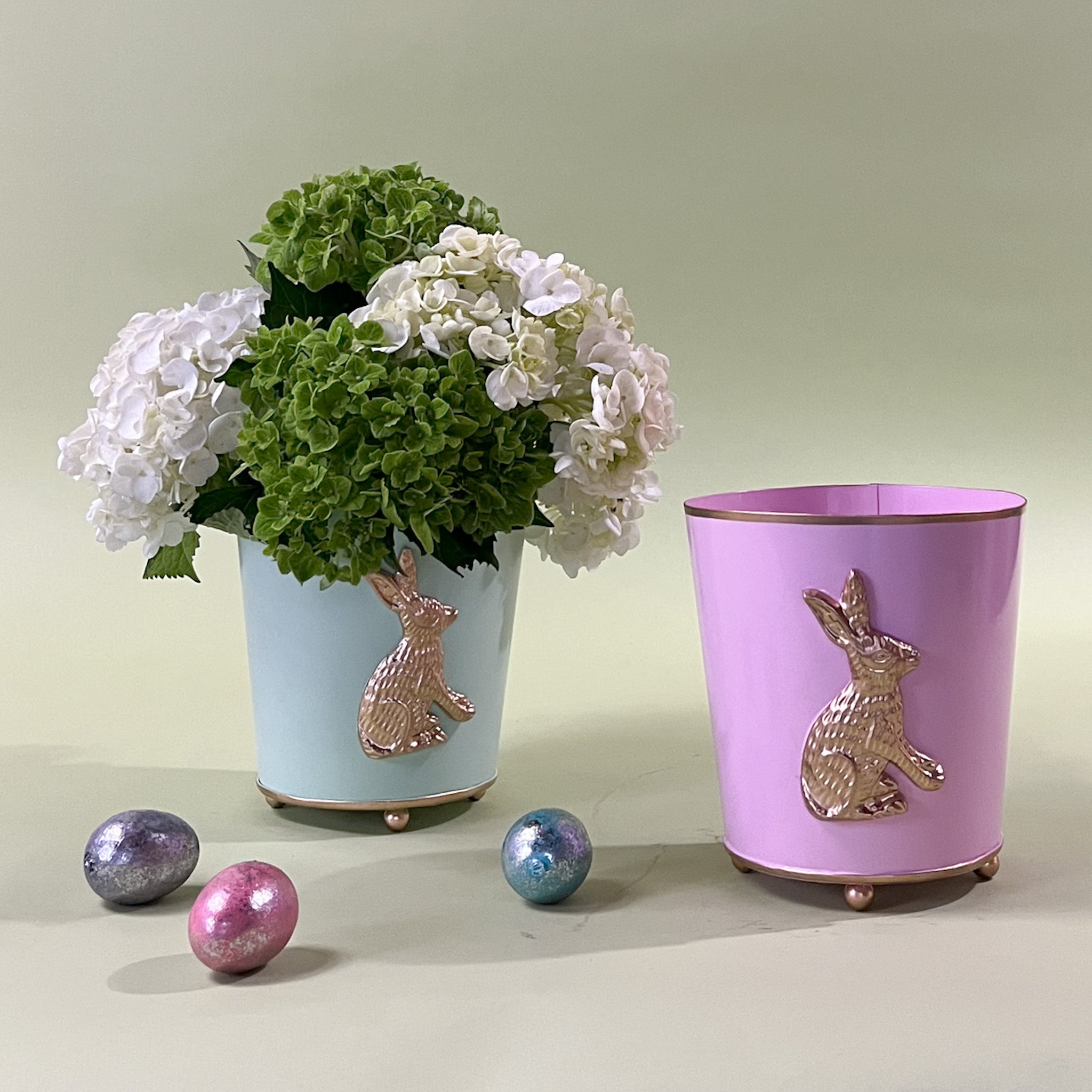 a green tole cachepot with a gold bunny motif and a pink tole cachepot with a bunny motif on a green background.