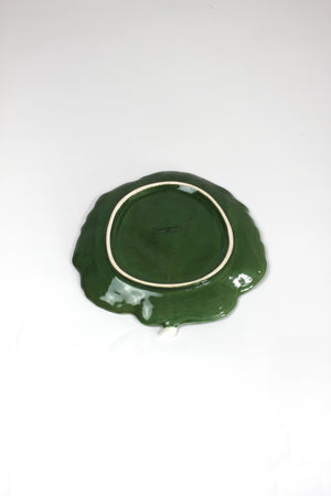 the underside of a ceramic green cabbage leaf plate on a white background.