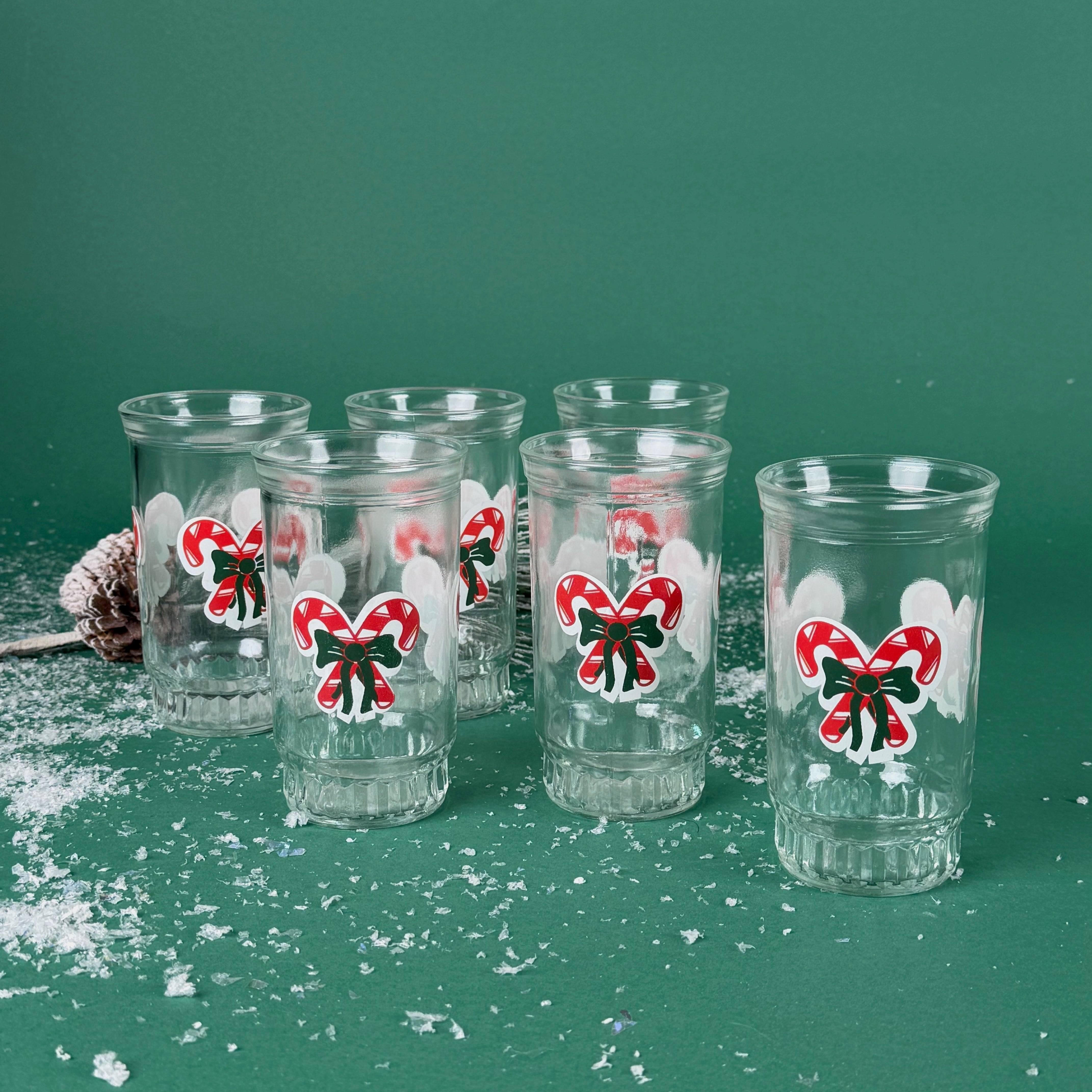 Set of six clear holiday tumblers with red candy cane bow designs on a snowy green background