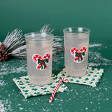 Two holiday tumblers with red candy cane bow design filled with a clear drink, placed on patterned coasters with faux snow and Christmas décor