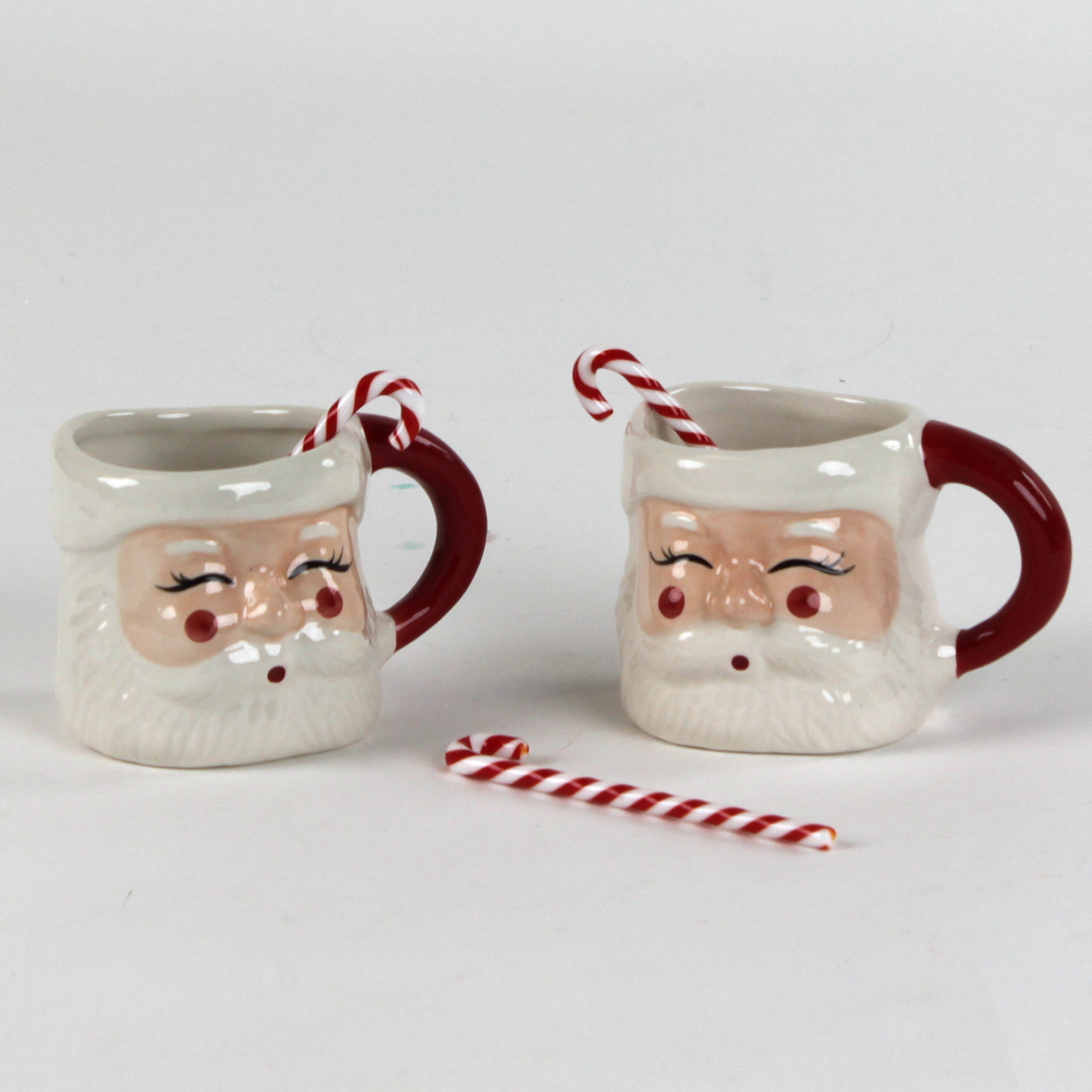 Two Santa Claus mugs with candy canes christmas swizzle sticks on a white background