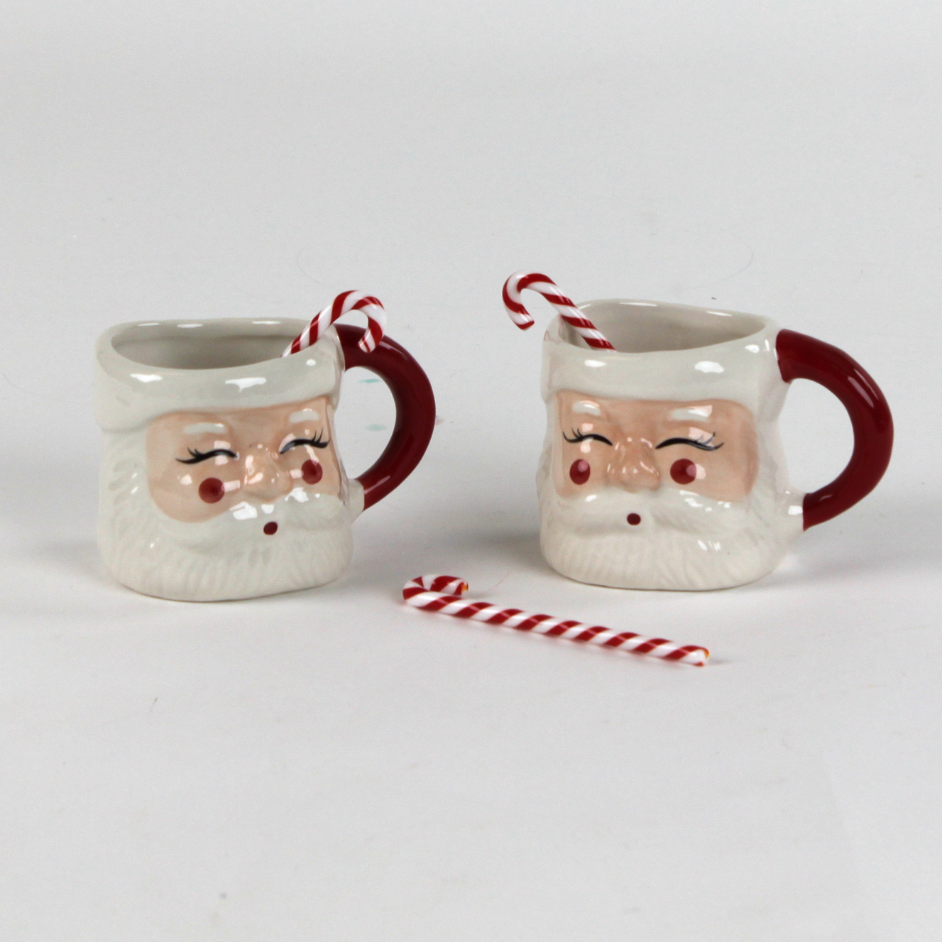 Two Santa Claus mugs with candy canes christmas swizzle sticks on a white background