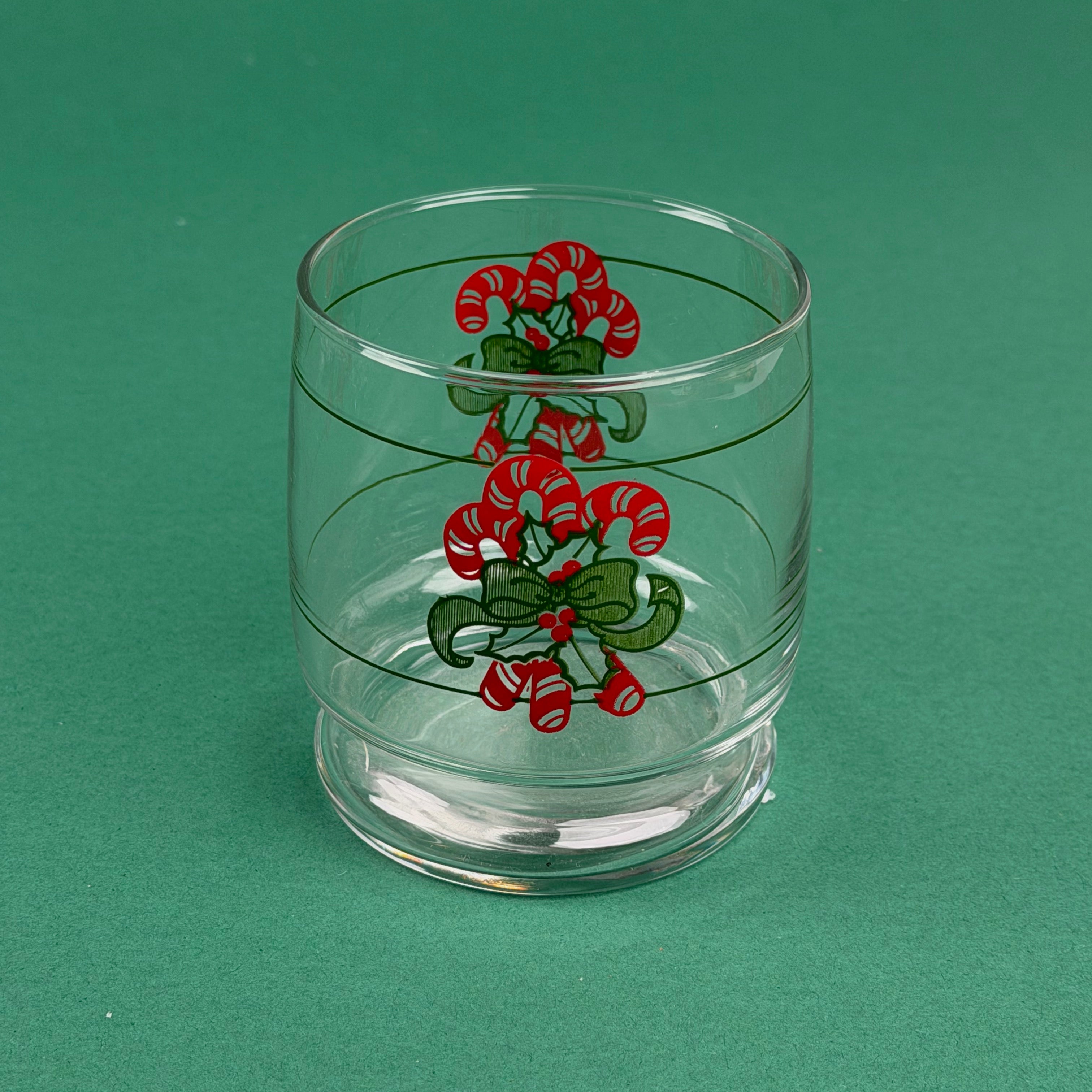 Clear holiday drinking glass with red candy cane and green ribbon design on a green background