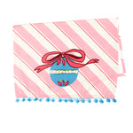 diagonally striped pink christmas tea towel with a large blue ornament motif at the bottom and blue pom pom trim against a white background. 