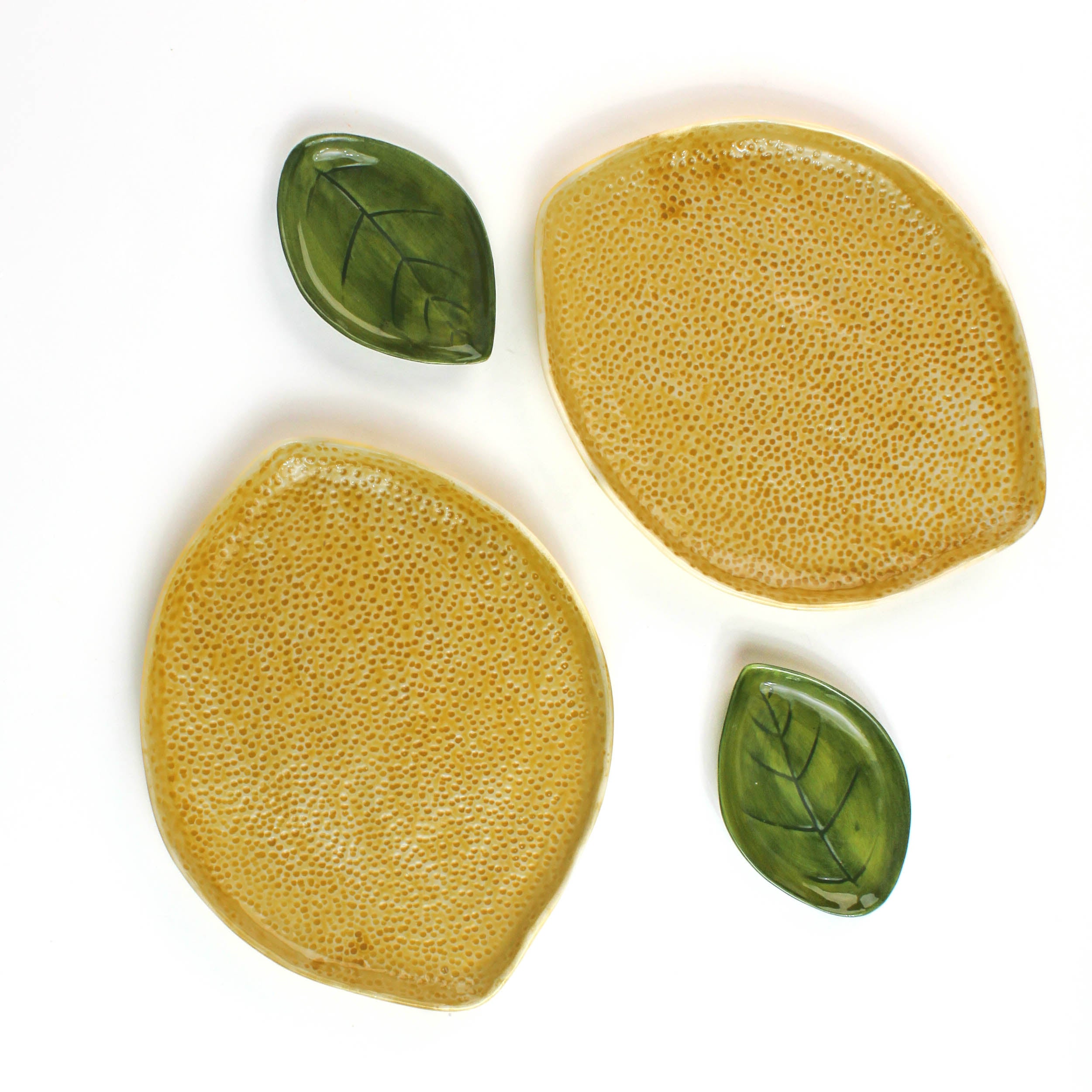 Two textured yellow lemon shaped plates  with two smaller matching green leaf shaped plates on a white background