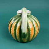 Green and orange ceramic pumpkin-shaped pitcher with a curved handle.