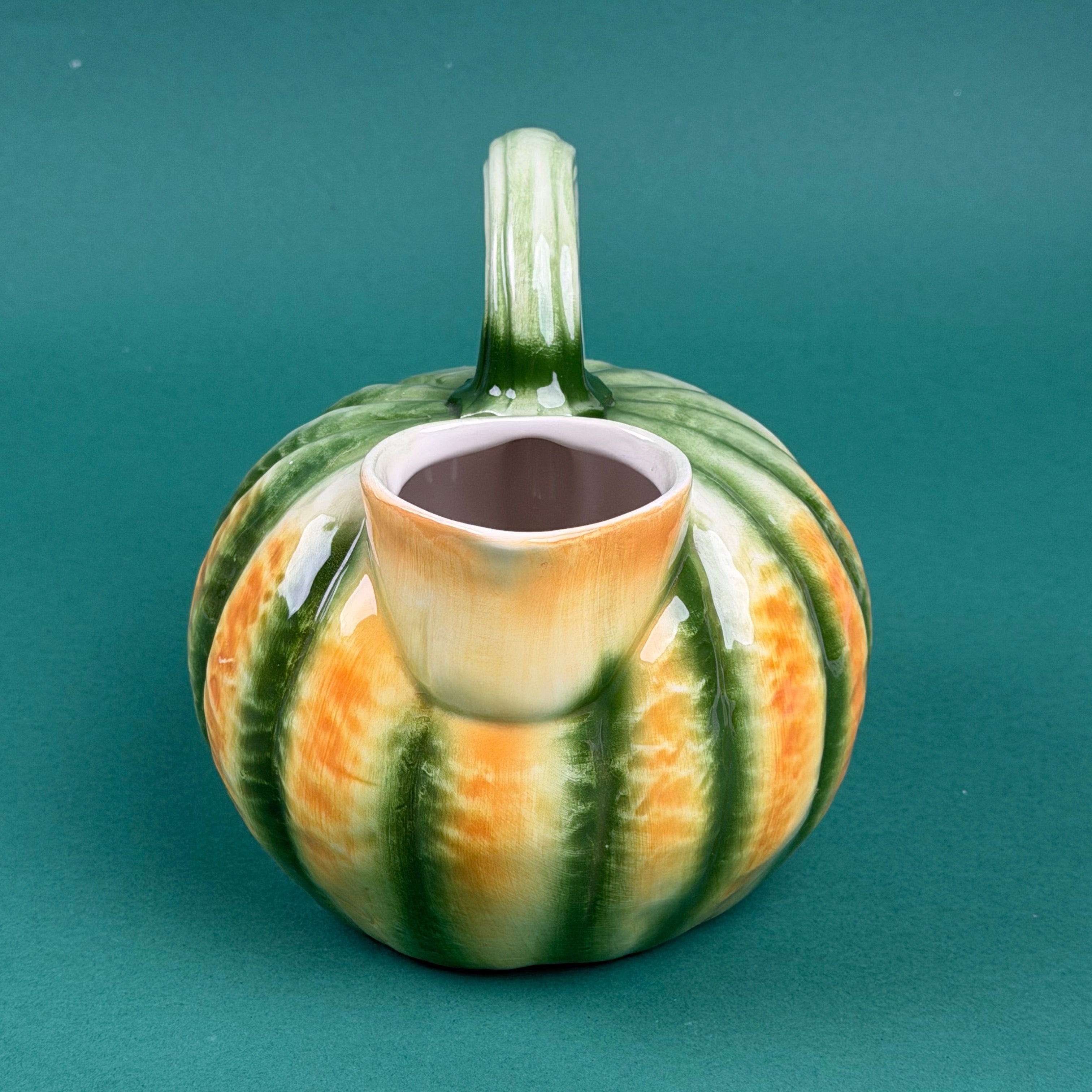 Green and orange ceramic pumpkin-shaped pitcher with a curved handle.