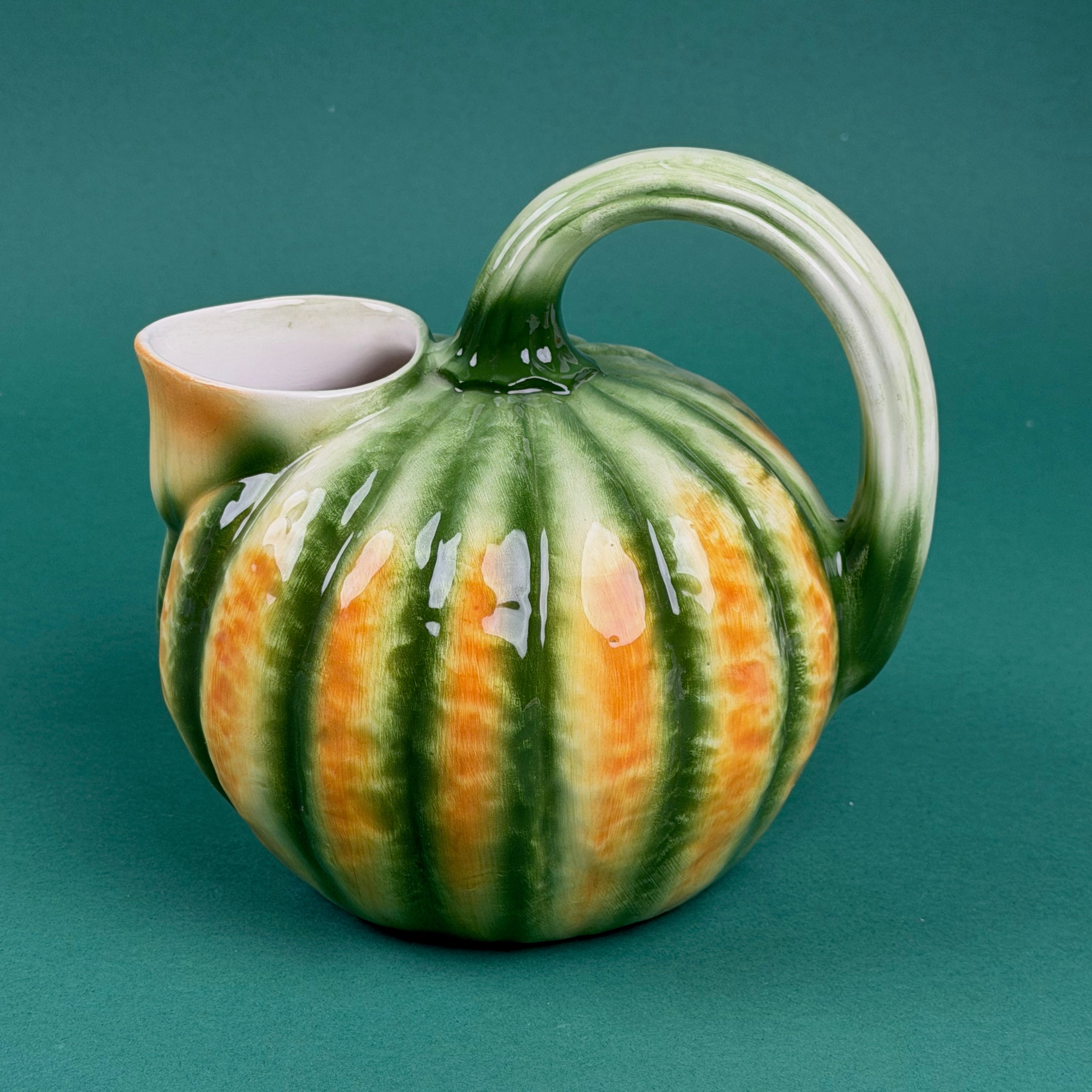 Green and orange ceramic pumpkin-shaped pitcher with a curved handle.