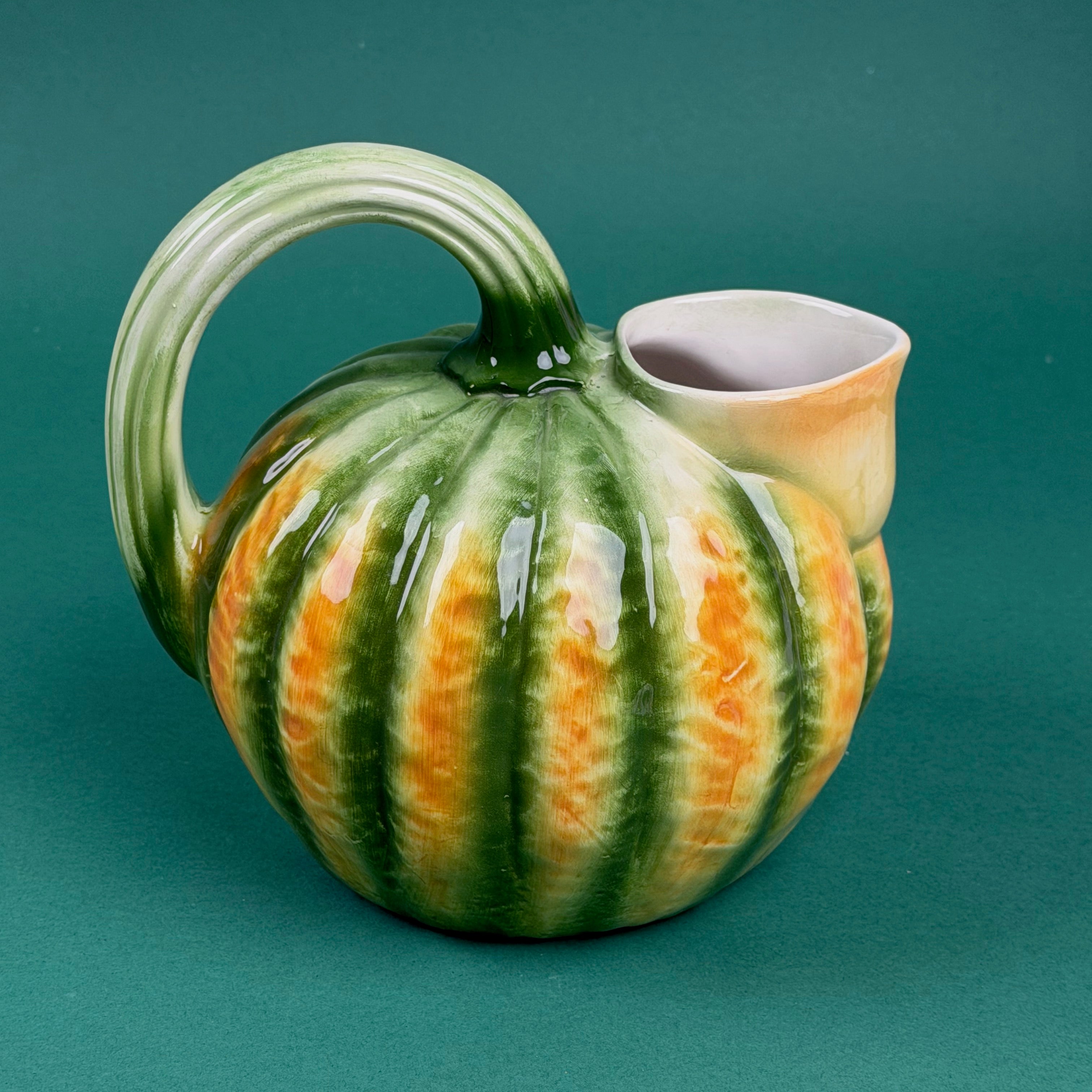 Green and orange ceramic pumpkin-shaped pitcher with a curved handle.
