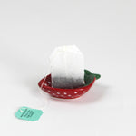a small red strawberry shaped ceramic bowl with a teabag resting in it. 