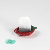 a small red strawberry shaped ceramic bowl with a teabag resting in it. 