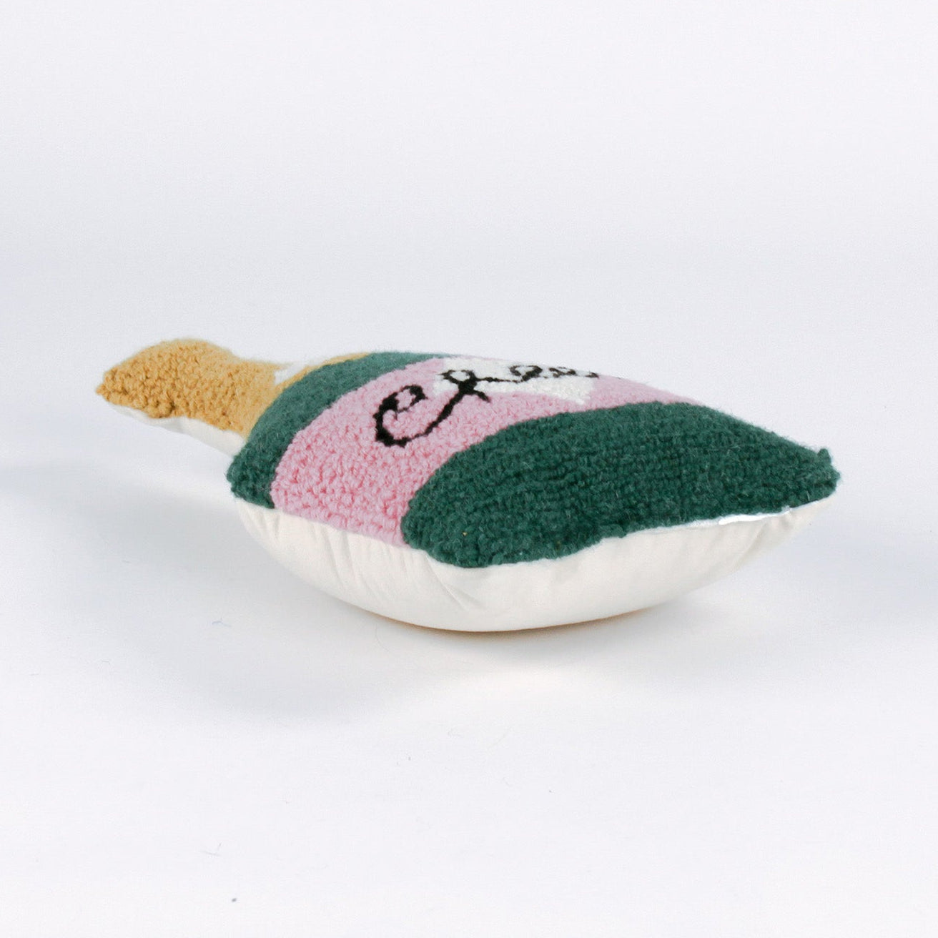 Bottle-shaped decorative pillow with a hooked texture, designed like a champagne bottle in green, pink, and gold colors, featuring the word “Cheers” on the label lying down a white background