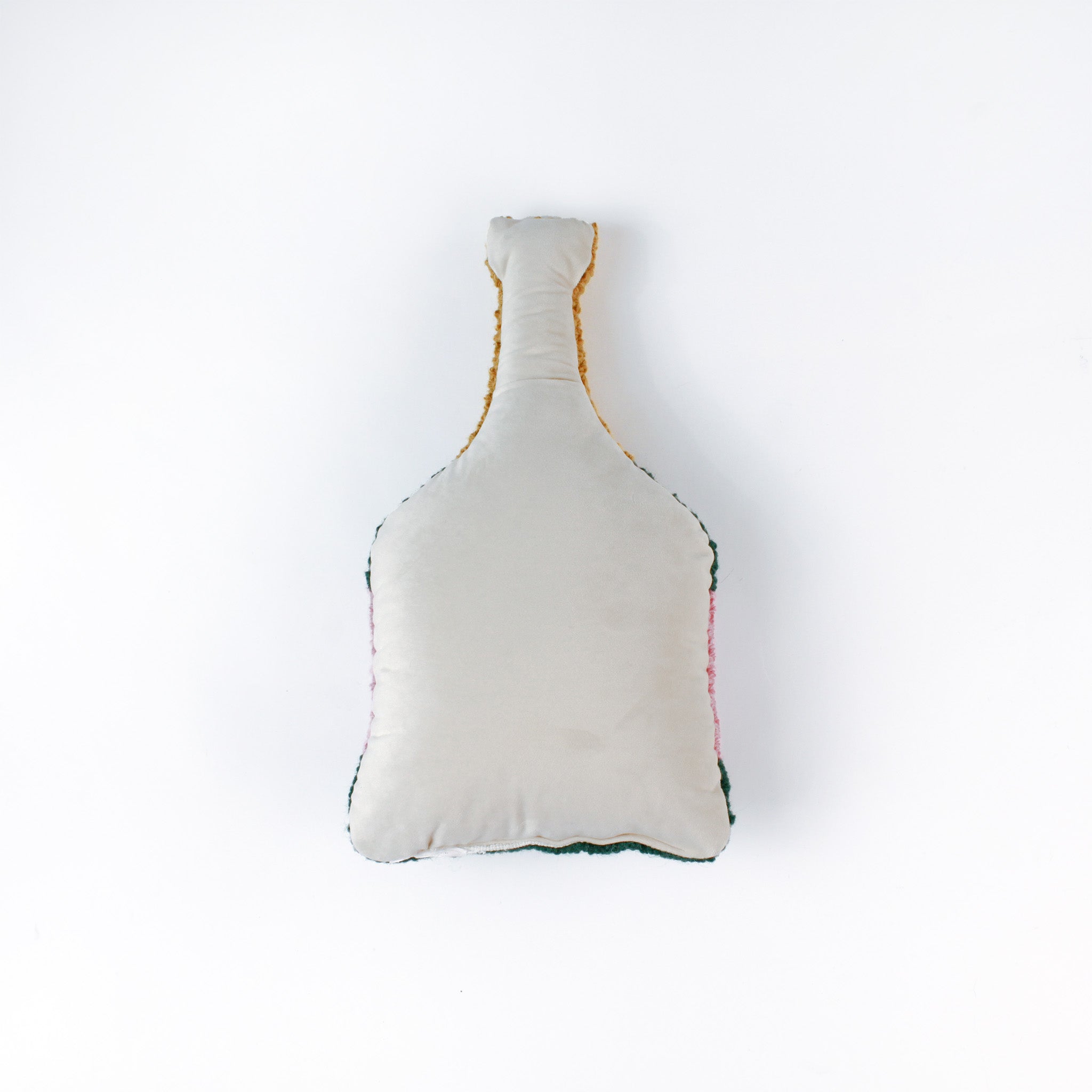 back of a bottle-shaped decorative pillow with a hooked texture, designed like a champagne bottle in green, pink, and gold colors, featuring the word “Cheers” on the label.