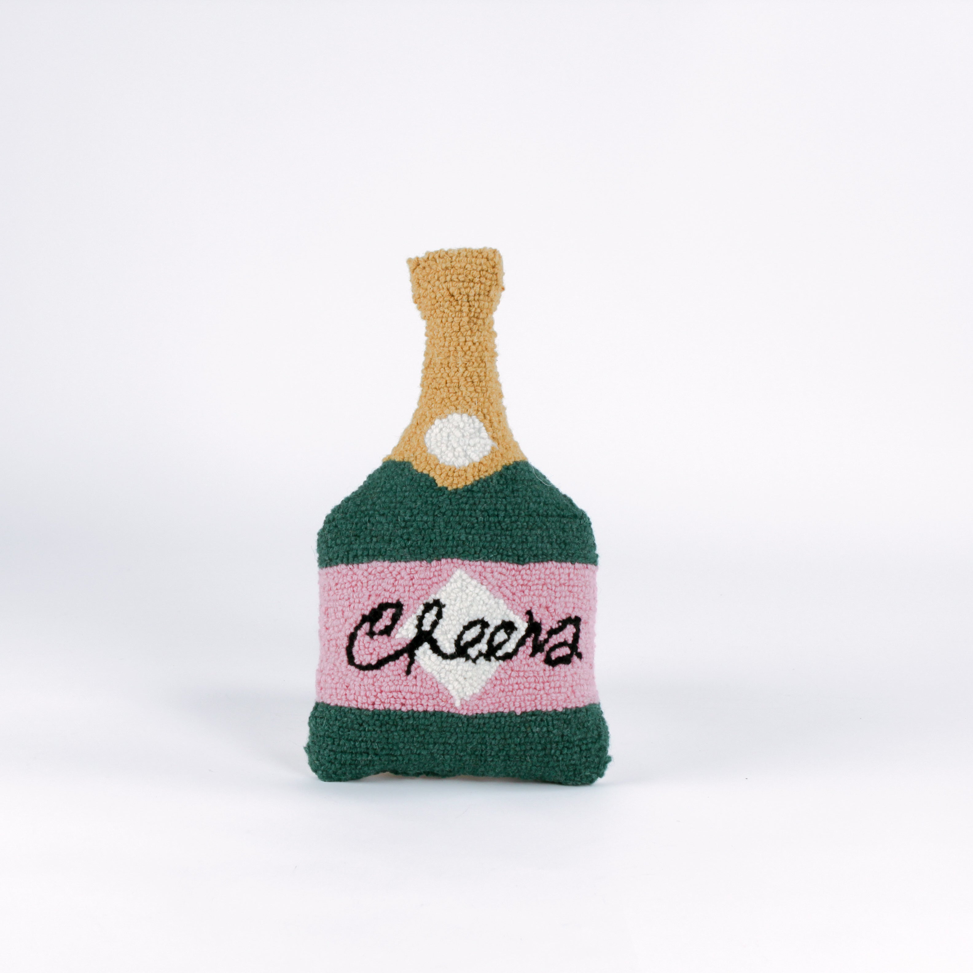 Bottle-shaped decorative pillow with a hooked texture, designed like a champagne bottle in green, pink, and gold colors, featuring the word “Cheers” on the label.