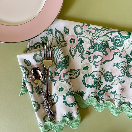 chinese dragon chinoiserie dinner napkins with green ric rac trim with cutlery on a green background