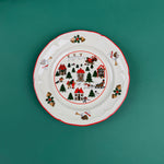 Christmas village-themed dinner plate with Santa, houses, trees, and holiday illustrations on a green background