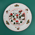 Christmas village-themed dinner plate with Santa, houses, trees, and holiday illustrations on a green background
