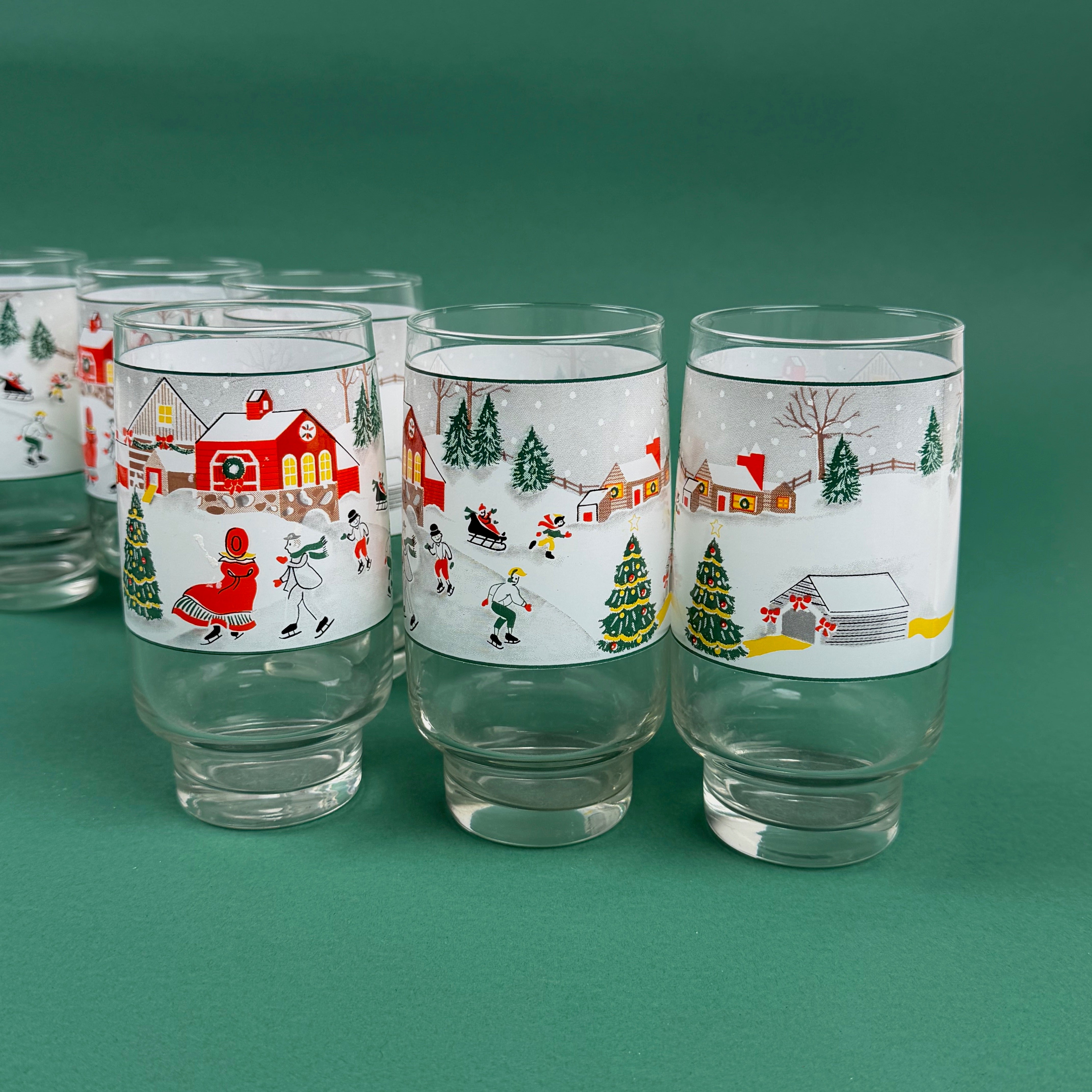 Set of Christmas village-themed drinking glasses with winter scenes on a green background