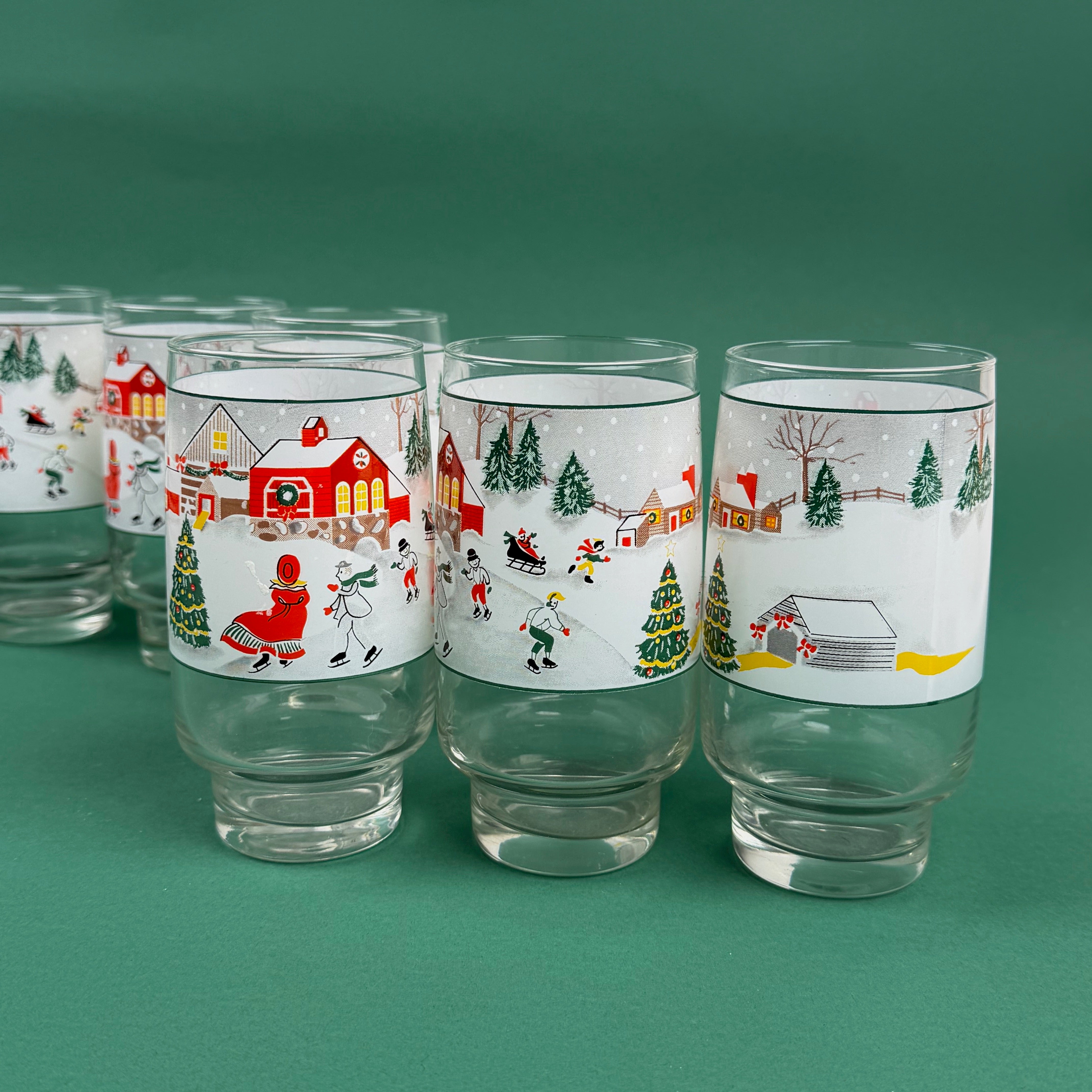 Set of Christmas village-themed drinking glasses with winter scenes on a green background
