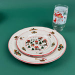 Stacked Christmas village-themed plates with a matching holiday glass on a green background