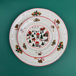 Stacked Christmas village-themed plates with red trim and holiday illustrations on a green background
