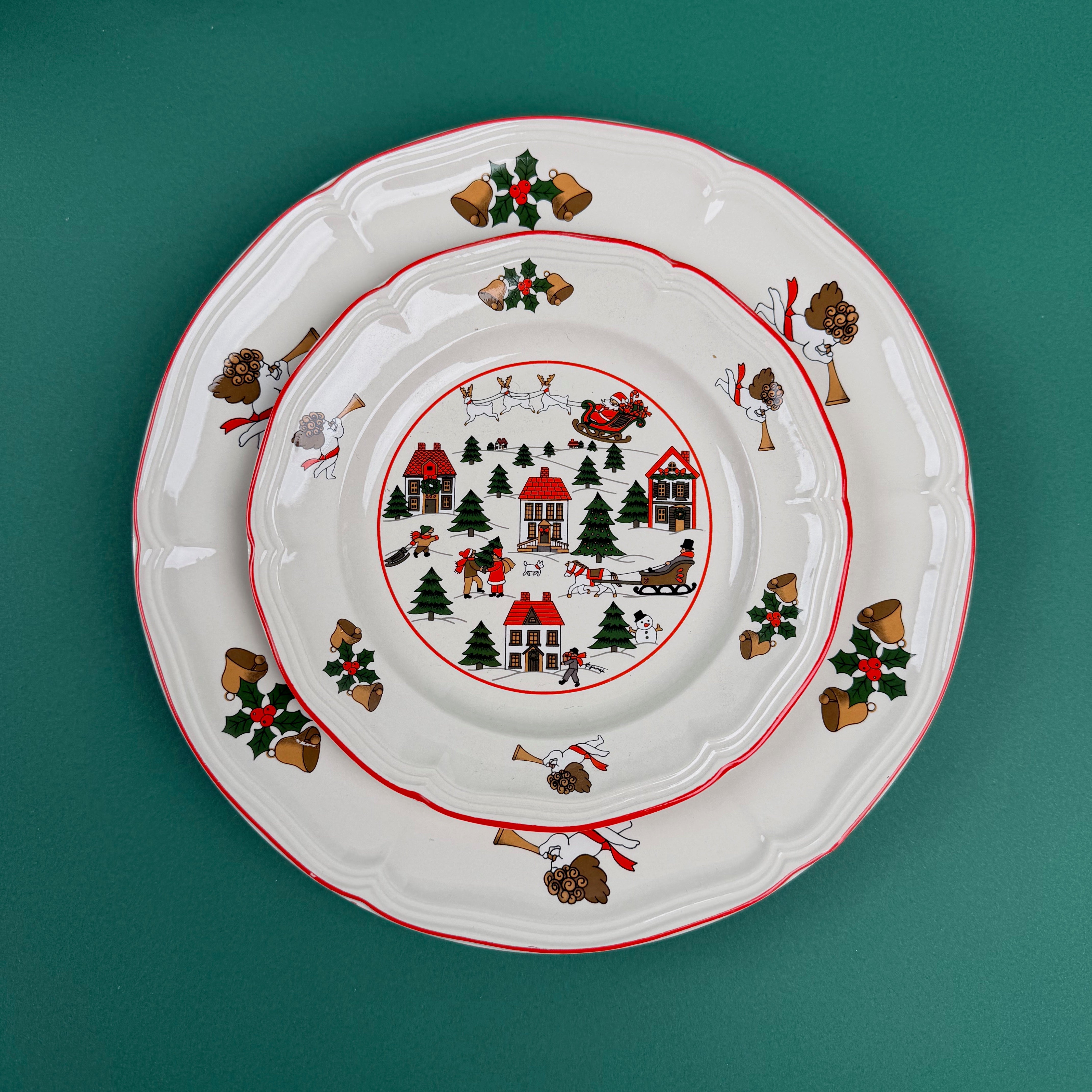 Stacked Christmas village-themed plates with red trim and holiday illustrations on a green background