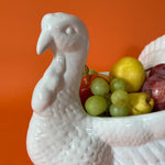 the face of a white ceramic turkey centerpiece filled with fruit