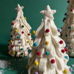 a set of three, white Looped Felt Christmas Tree Table Decorations with colourful bauble decorations, topped with stars against a green, snow scattered background. 