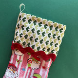 A pink christmas stocking made from pink santa motif fabric and a green patterned top with red ric rac trim