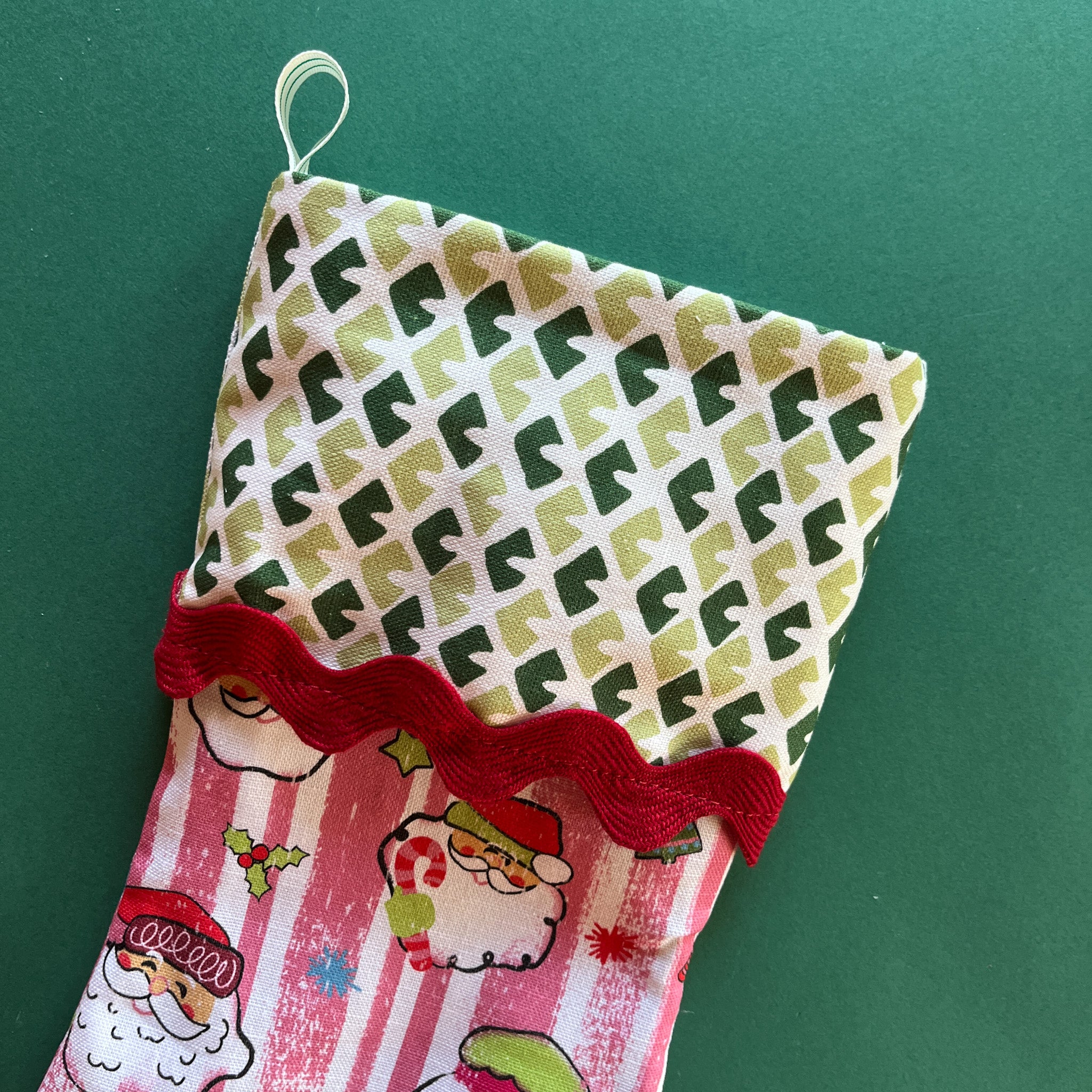 A pink christmas stocking made from pink santa motif fabric and a green patterned top with red ric rac trim