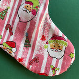 A pink christmas stocking made from pink santa motif fabric and a green patterned top with red ric rac trim