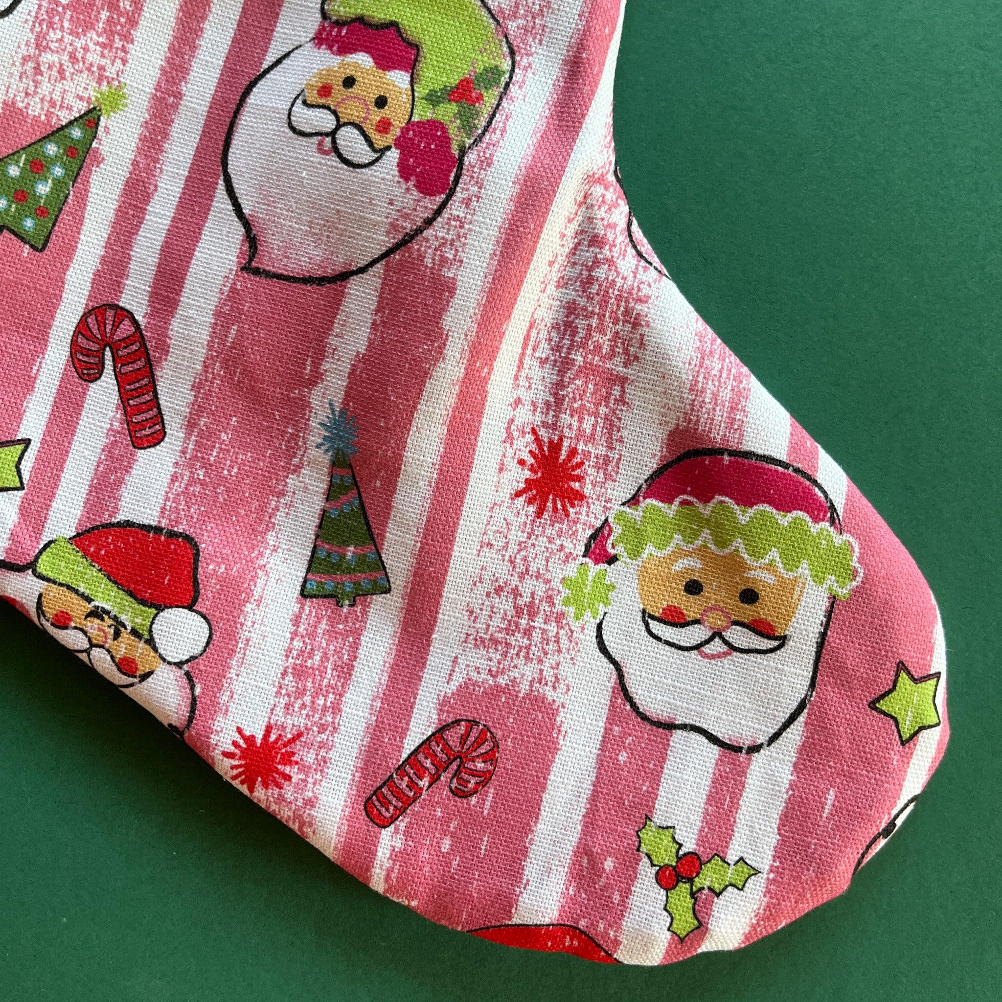 A pink christmas stocking made from pink santa motif fabric and a green patterned top with red ric rac trim