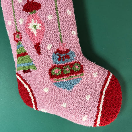 the toe of a hooked wool pink Christmas stocking with ornament motifs on it. 