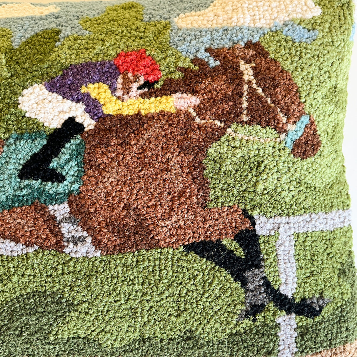 a close up of a derby day pillow featuring a horse and a jockey. 