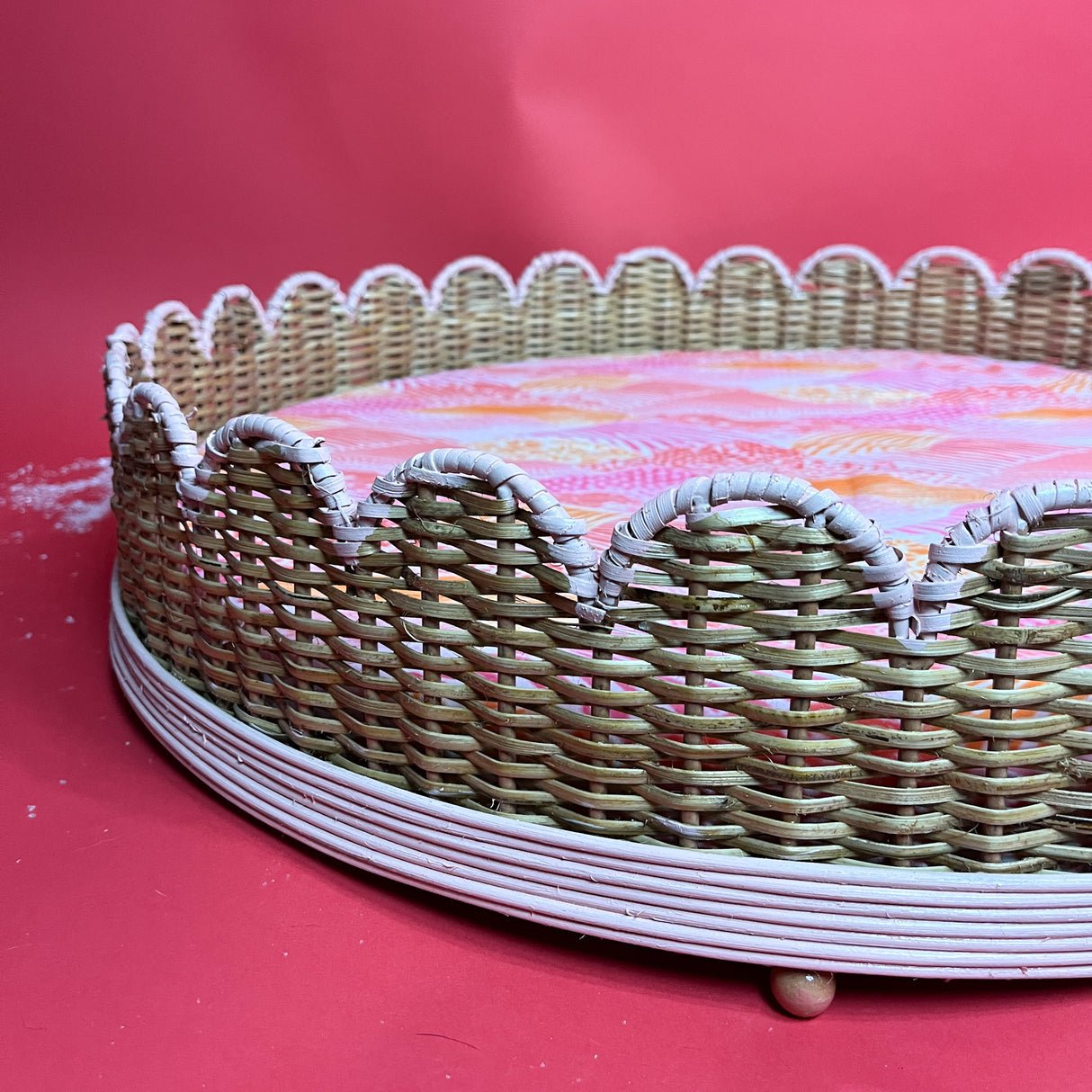 a close up of a scalloped rattan dog bed that is trimmed in pink.