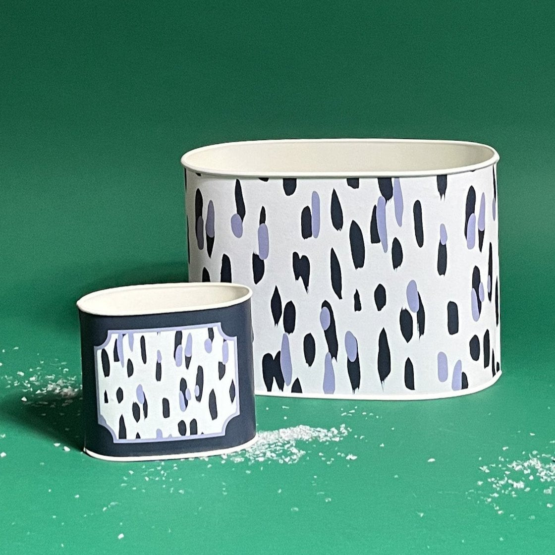 Two decoupage caddies with a navy blue and white animal print pattern, one large and one small, with a trail of white decorative snow on the floor.