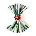 Green brush stroke patterned dinner napkin folded and styled with a red floral napkin ring, arranged for an elegant table setting and coordinated with a Christmas tea towel.