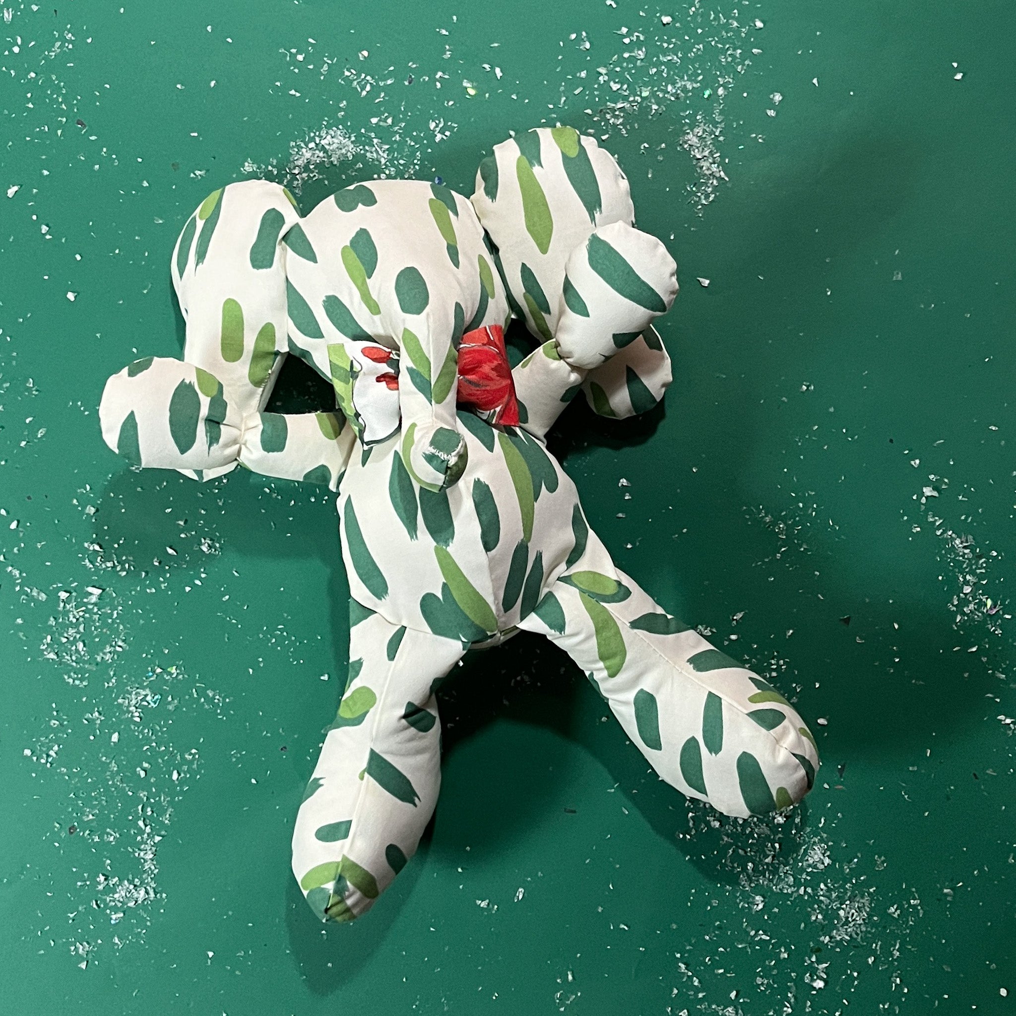 White stuffed elephant toy with green brushstroke pattern and red bow with green background.