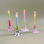 Four ceramic candle holders with scalloped edges holding pastel taper candles with four different patterns