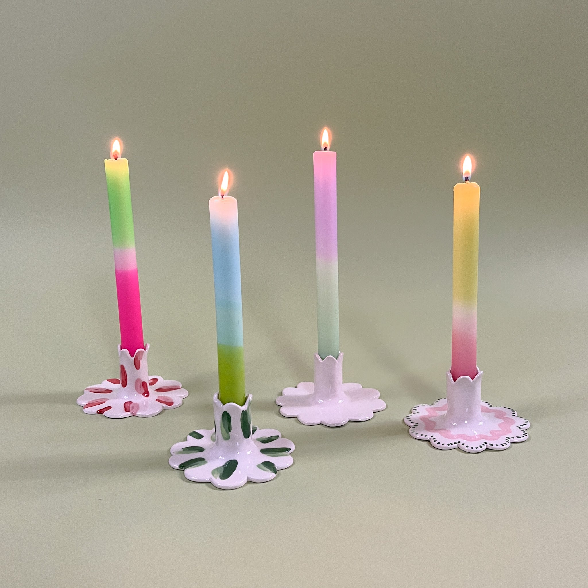 Four ceramic candle holders with scalloped edges holding pastel taper candles with four different patterns